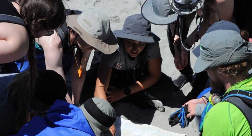 A group of people wearing sun hats and life jackets examine a map on the ground